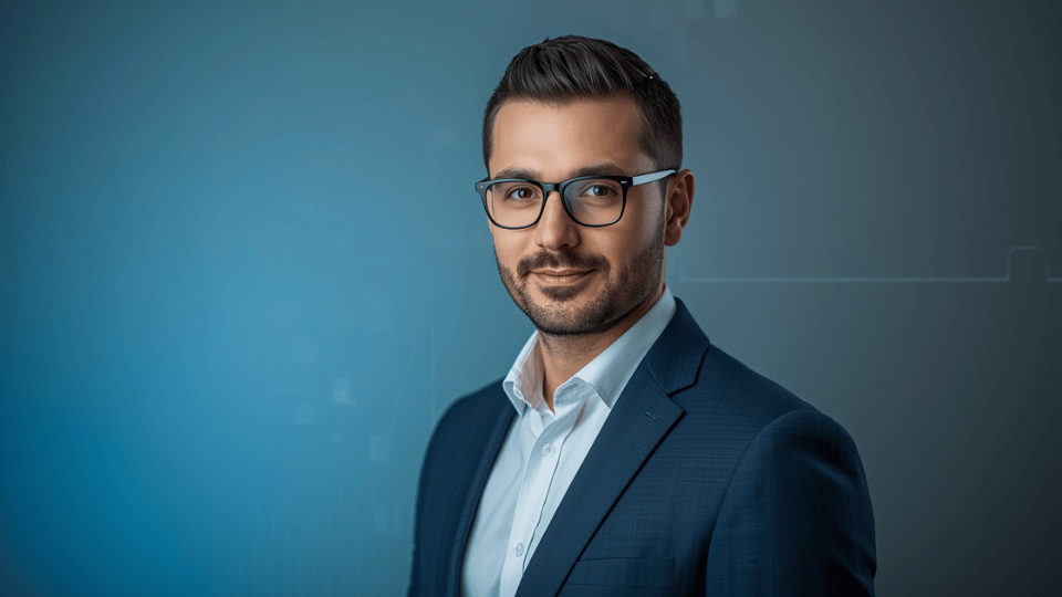 A professional portrait of a business owner in a blue suit jacket and glasses against a modern blue and grey studio backdrop.