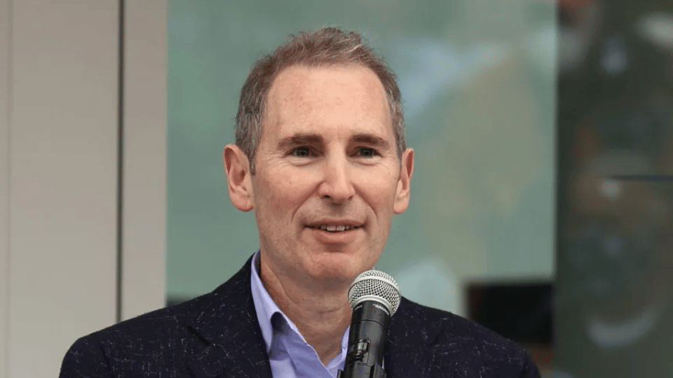A realistic photograph of a tech executive speaking into a microphone at a formal corporate media event.