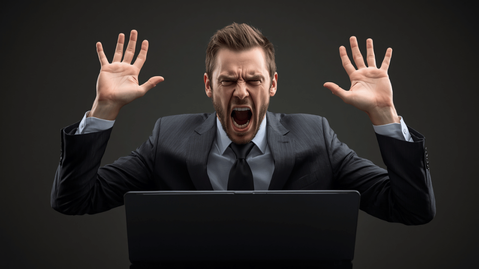 A frustrated man in a suit screams at his laptop screen