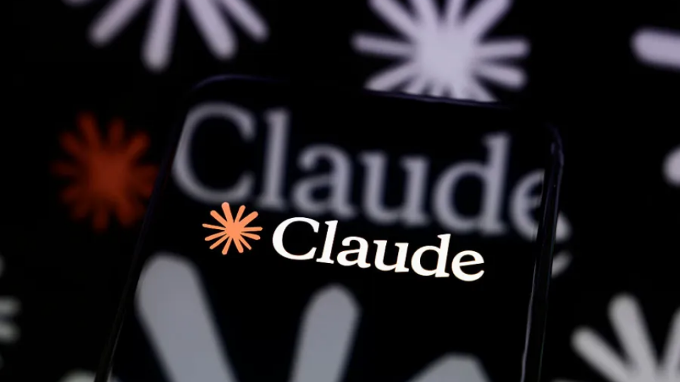 A close-up view of a glowing smartphone screen displaying the white Claude application logo against a dark background with blurred starburst shapes.
