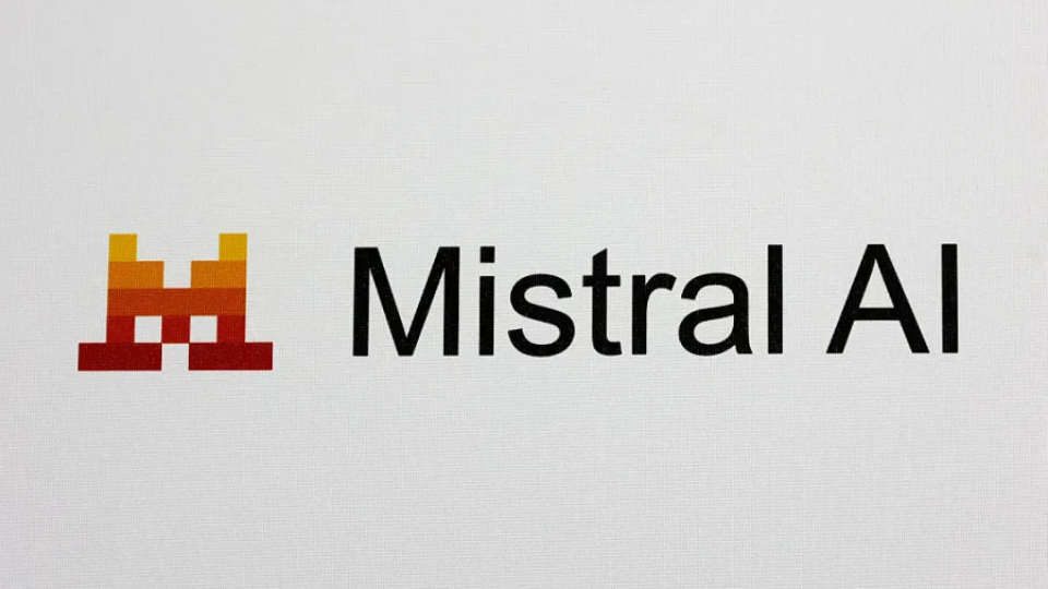 A close-up view of the orange and red geometric Mistral AI corporate logo mounted on a clean grey office wall.
