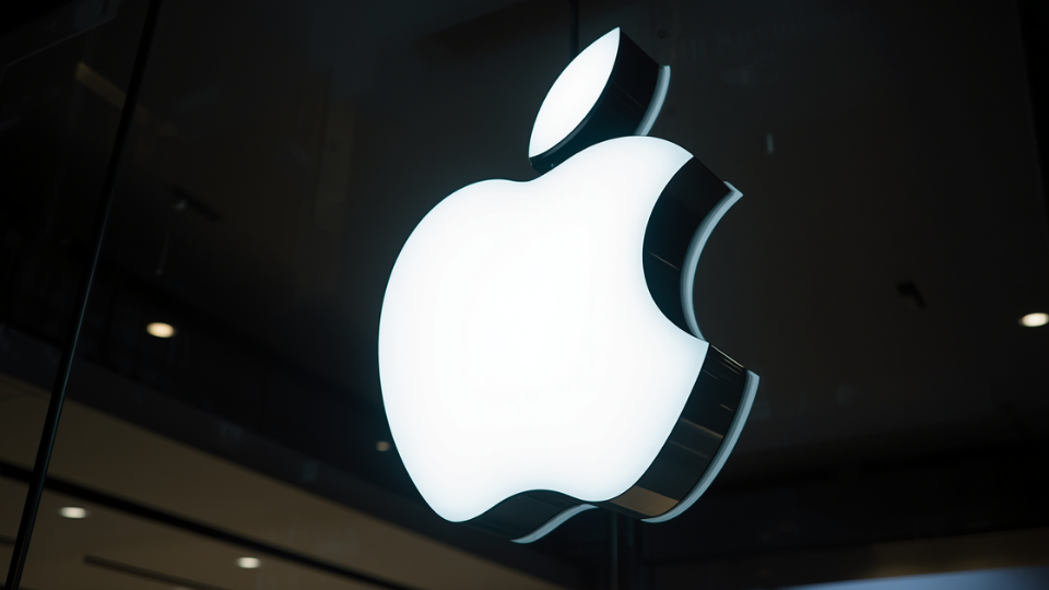 A close-up view of a large glowing white Apple logo mounted on a modern glass storefront at night.