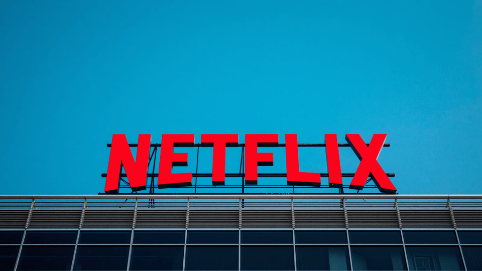 A large red Netflix sign mounted on top of a building structure under a clear blue sky.
