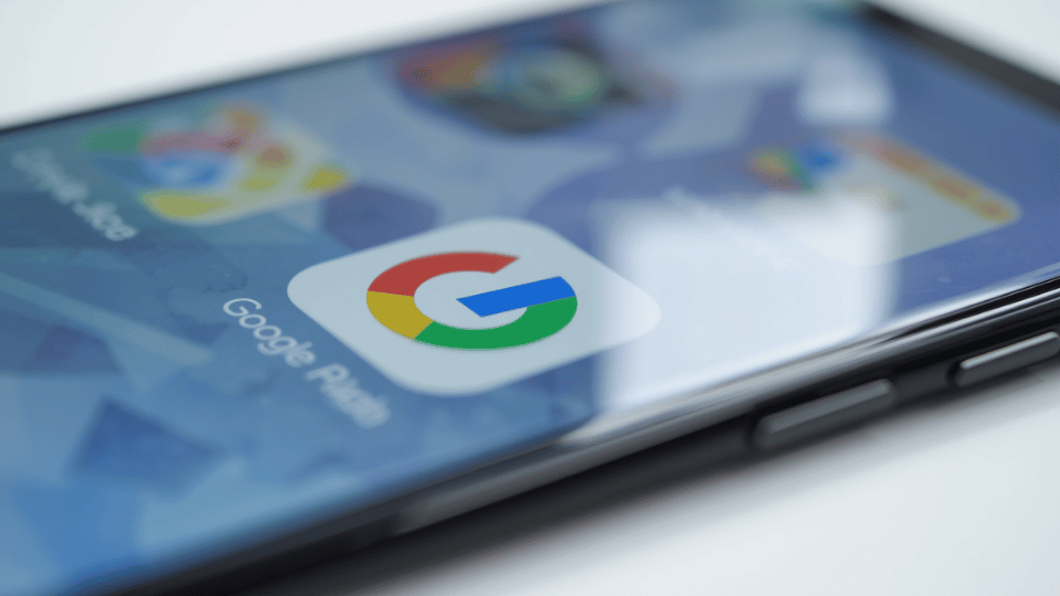 A close-up view of a smartphone screen displaying a sharp Google app icon with other blurred mobile apps in the background.