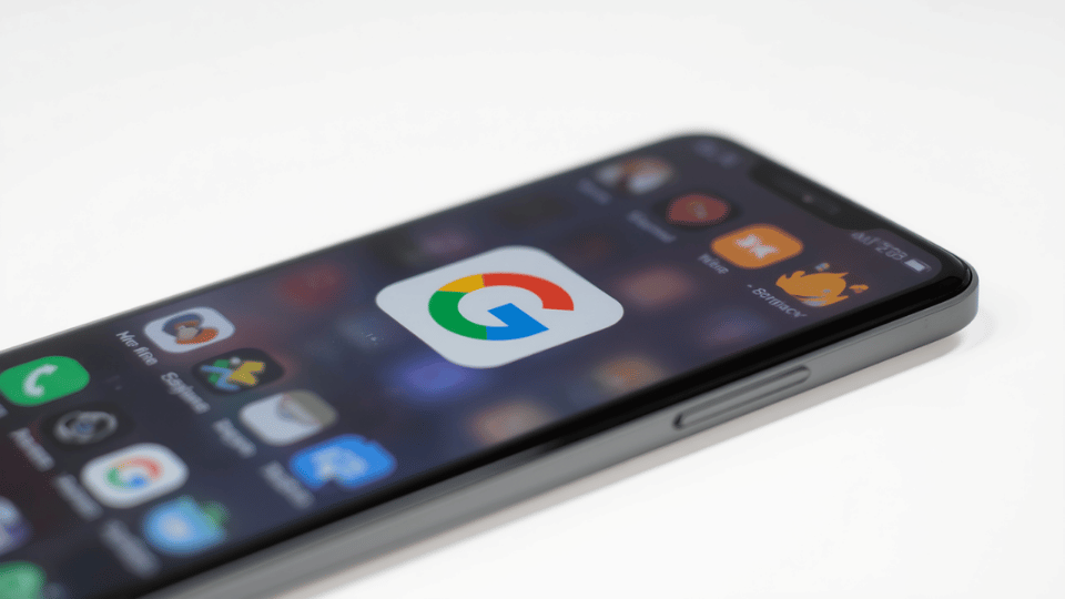 A close-up view of a smartphone display showcasing the multi-colored Google logo icon with blurred mobile apps in the background.