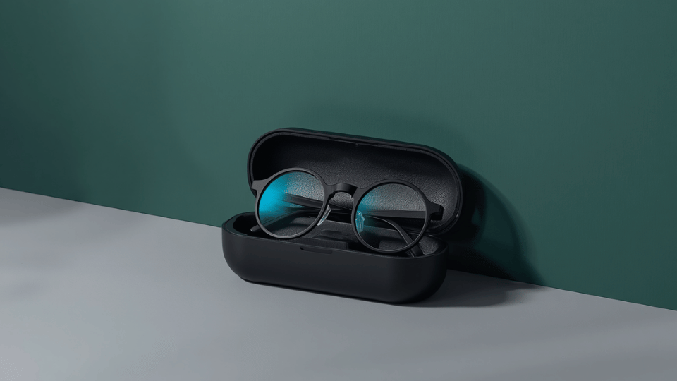 A pair of minimalist black-framed smart glasses with clear lenses resting inside a black protective case against a clean studio background.