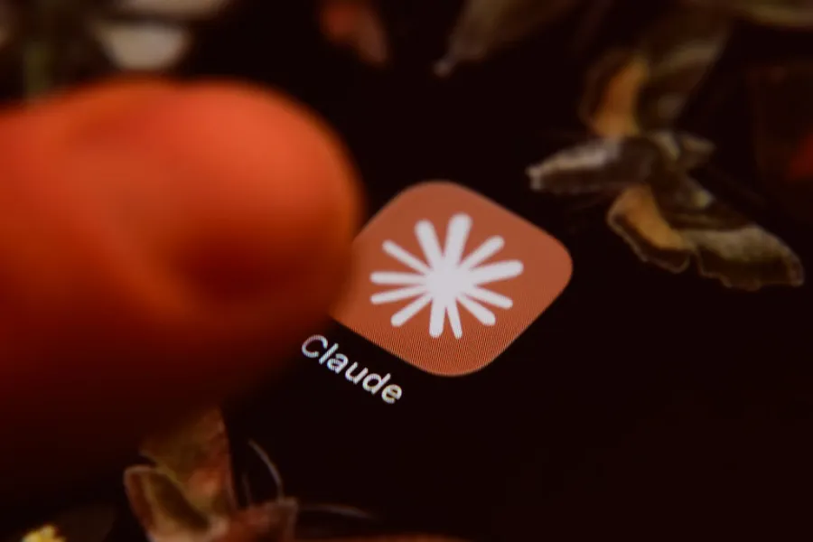A close-up view of a glowing smartphone screen displaying an orange application icon with a white star logo and the word Claude.
