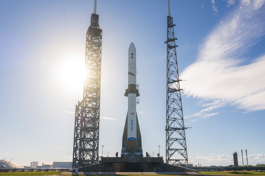 A massive white orbital rocket standing tall on a launch pad between two giant metal towers under a clear sky.