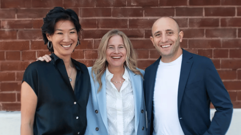 Three Reach Capital partners smiling together while standing in front of a red brick wall.