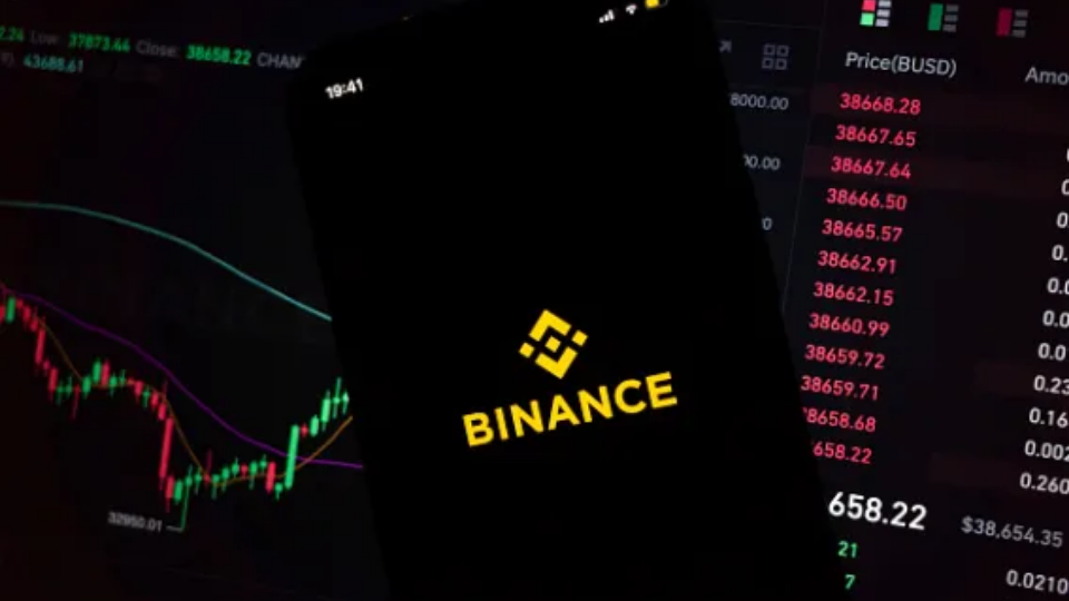 A smartphone screen displaying the Binance logo against a green financial chart background.