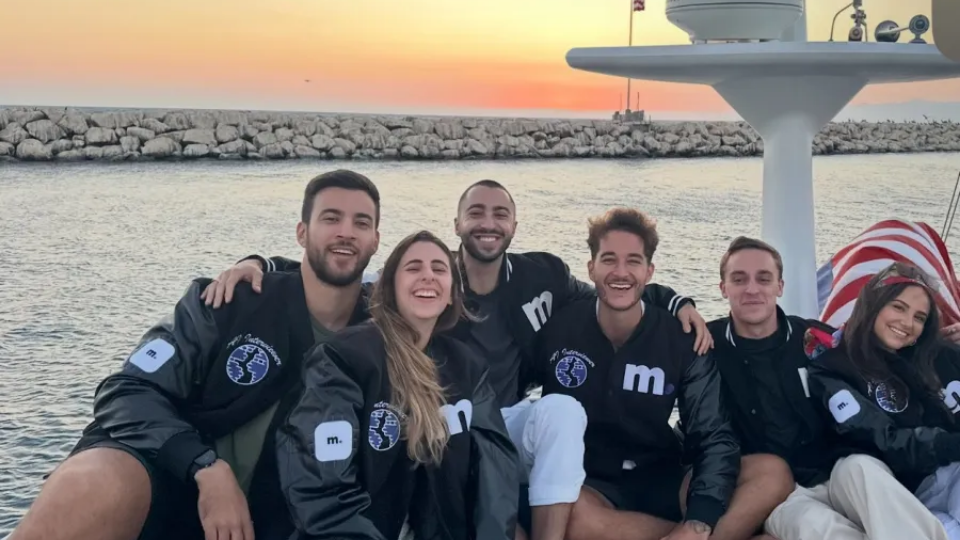A group of Micro1 team members posing together on a boat deck during sunset.