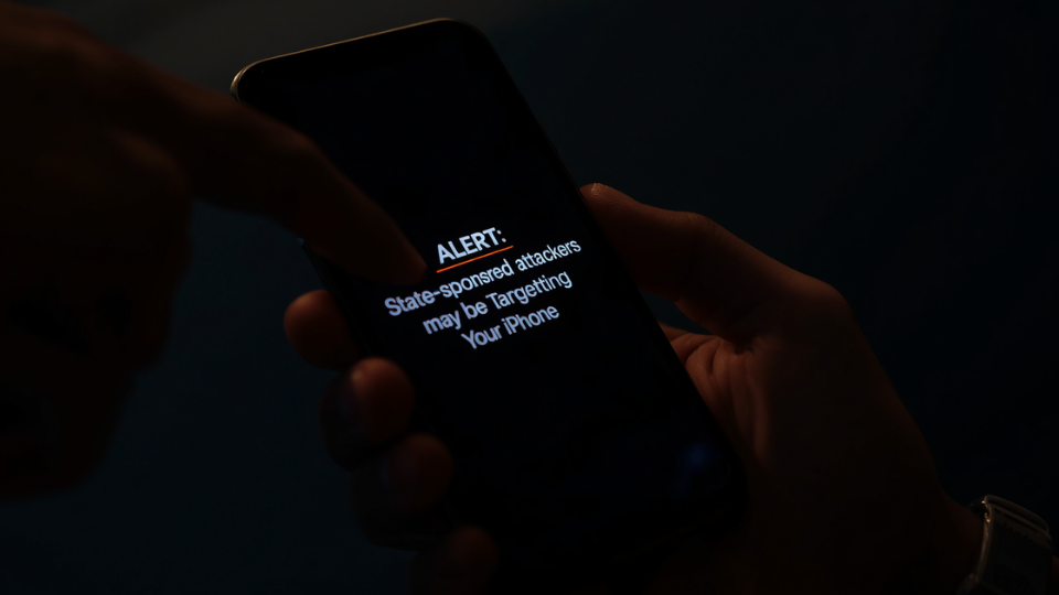A hand holding a smartphone displaying a state-sponsored spyware warning notification on screen.