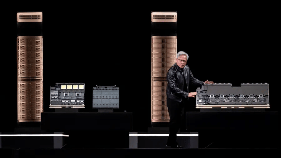 Jensen Huang presenting on stage with a large server rack displayed behind him.