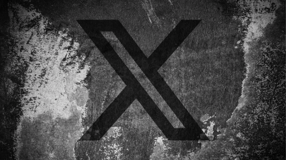 A black stylized letter X spray painted onto a dark textured concrete surface.