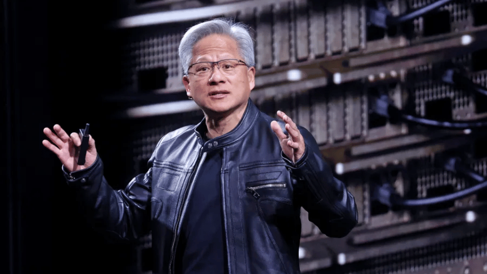 Nvidia CEO Jensen Huang speaking on stage wearing a black leather jacket in front of server racks.
