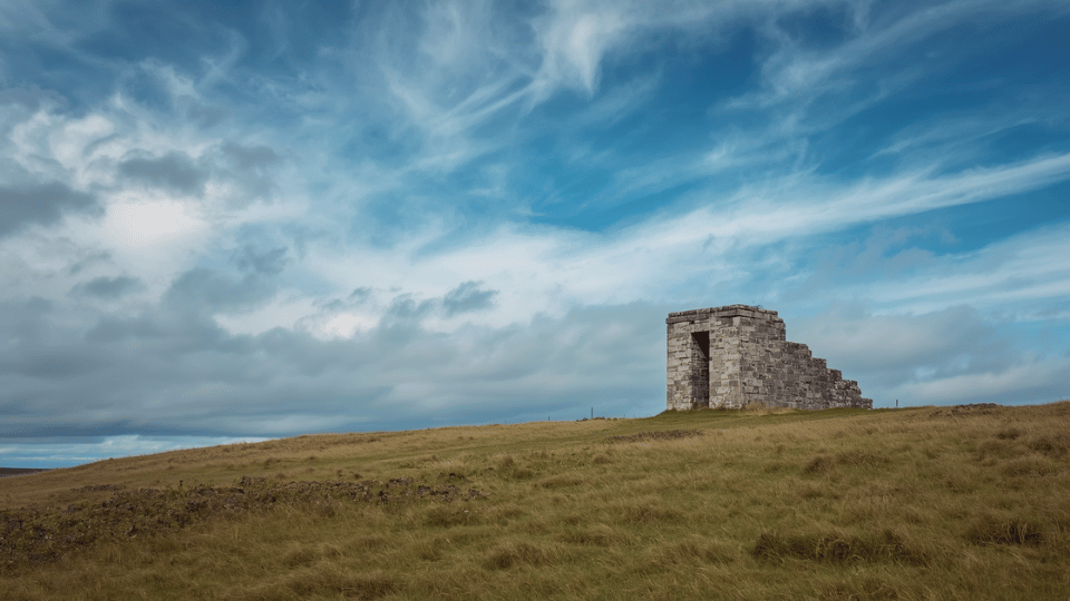 A lonely weathered concrete structure standing in a grassy field under a cloudy sky.