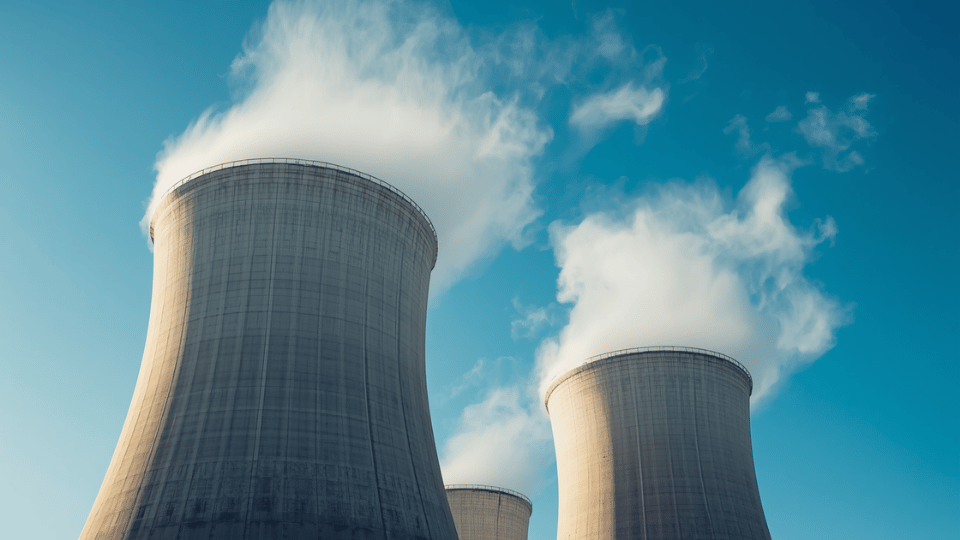 Concrete nuclear cooling towers venting clean steam against a bright blue sky.