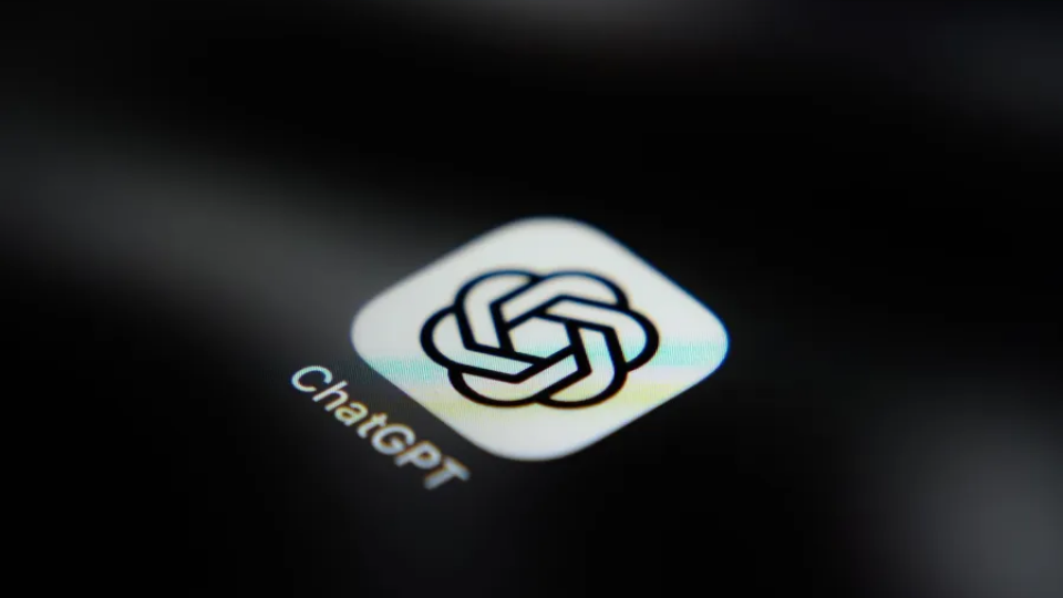 A smartphone displaying the ChatGPT logo on a dark surface with blue accent lighting.